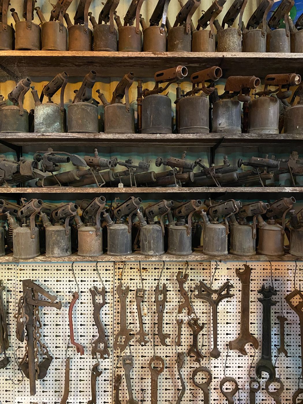 Four shelves of kerosene blowtorches above spanners on pegboard